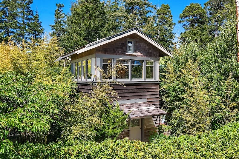 A serene coastal cabin nestled among lush greenery under a clear blue sky offers a tranquil retreat for nature lovers seeking a peaceful getaway.