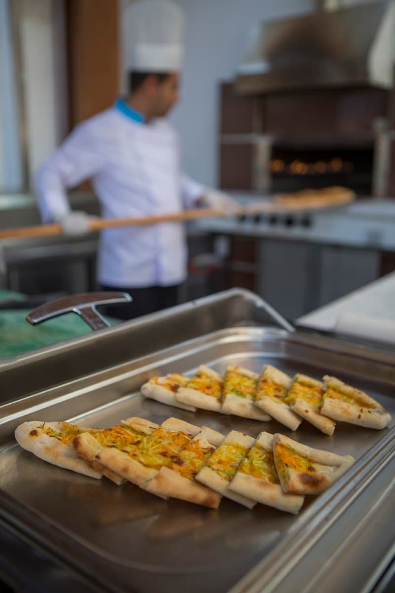 A chef in a bustling kitchen prepares freshly baked flatbreads on a tray, capturing the inviting culinary atmosphere of a resort dining experience at Seashell Resort & Spa in Antalya, Turkey.