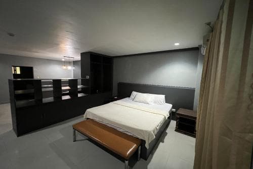 A modern hotel room features a neatly made bed with white linens, a sleek black storage unit, and a cozy bench, creating a minimalist and inviting atmosphere ideal for travelers seeking comfort and simplicity.