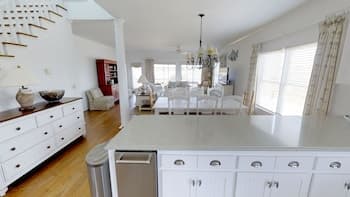 A bright, spacious kitchen with white cabinetry, hardwood floors, and large windows creates an inviting atmosphere, perfect for family gatherings or a cozy retreat during a vacation rental stay.