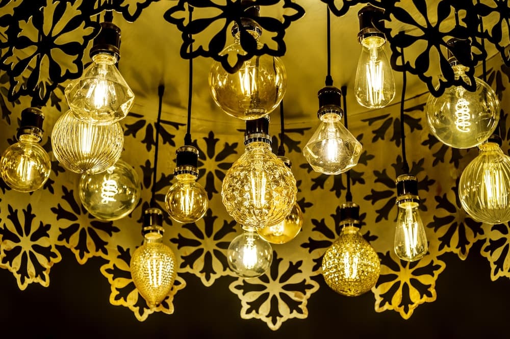 A cozy indoor space features an array of vintage-style light bulbs hanging from intricate metalwork, creating a warm and inviting ambiance ideal for intimate gatherings or photography backdrops.