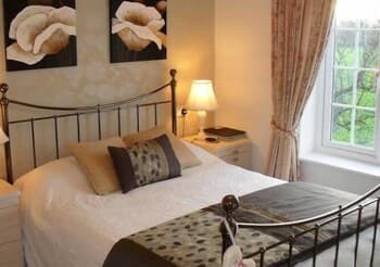 A cozy bedroom with a neatly made bed, floral artwork, and a bright window view of greenery, ideal for travelers seeking a serene and inviting accommodation experience.