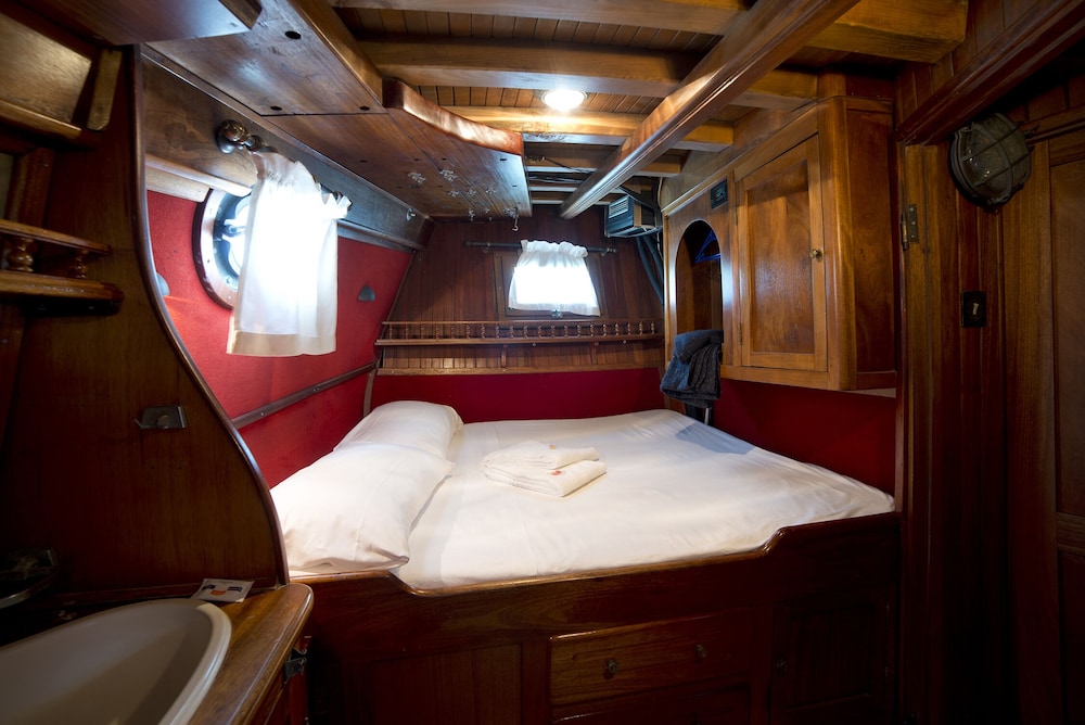 A cozy cabin interior with polished wood paneling, a neatly made bed, and porthole windows offers a serene retreat for travelers seeking a nautical adventure.