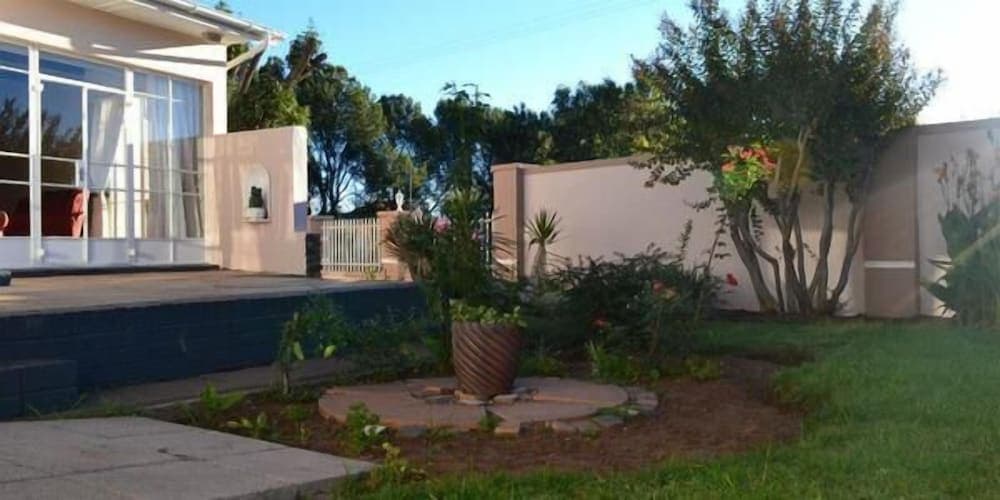 A serene suburban garden features lush greenery, a central potted plant, and a modern house with large windows, ideal for travelers seeking a peaceful retreat in a residential area.