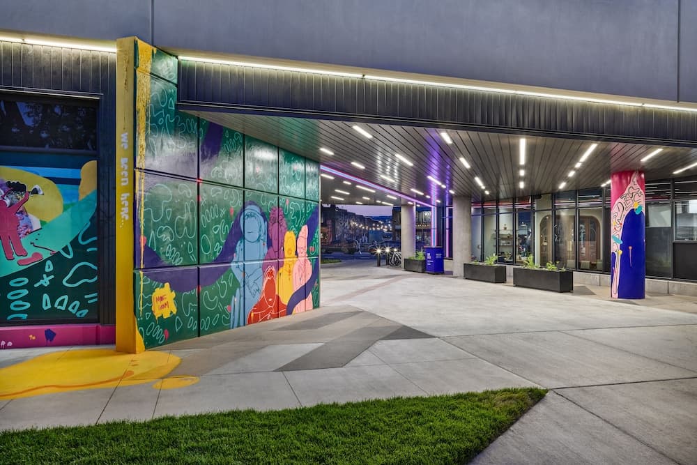 A vibrant urban plaza features colorful murals, modern architecture, and illuminated walkways, creating an inviting atmosphere ideal for evening strolls and cultural exploration.