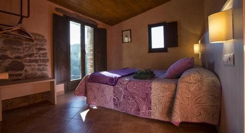 A cozy bedroom with rustic charm features a patterned bedspread, wooden floors, stone walls, and warm lighting, ideal for travelers seeking a serene retreat in a countryside lodge.