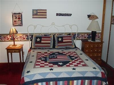 A cozy bedroom adorned with patriotic American flag-themed decor, featuring a quilted bedspread, matching pillows, and framed flags, creates a warm and inviting atmosphere ideal for travelers seeking a themed accommodation experience.