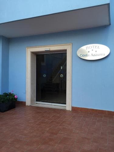 A serene hotel entrance with a glass door framed by blue walls and a tiled patio, featuring a "Hotel Costa Azzurra" sign, ideal for travelers seeking coastal accommodations.