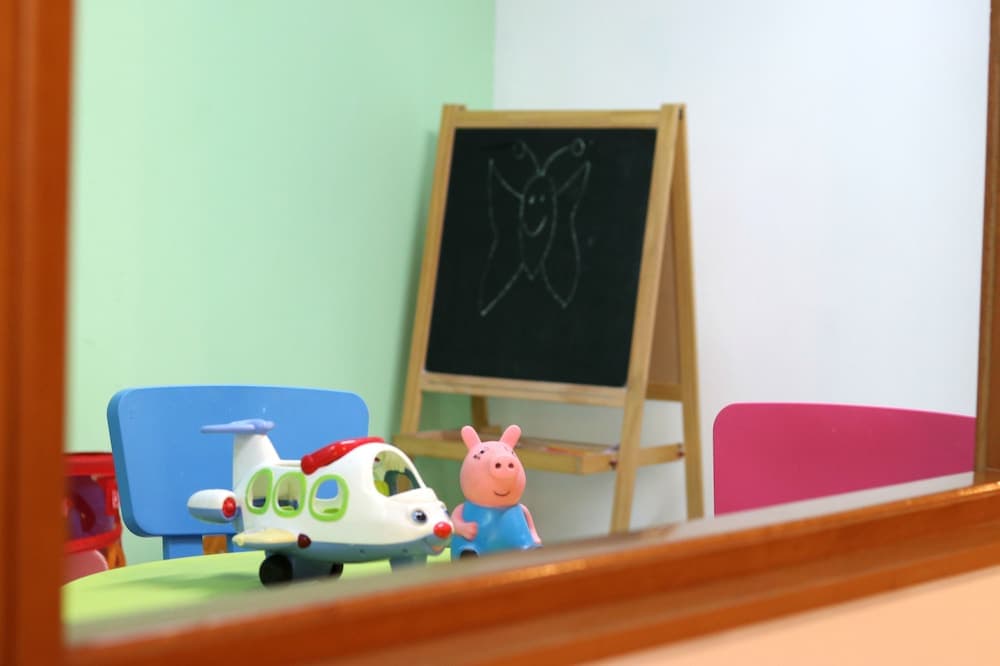 A cozy children's playroom reflected in a mirror showcases colorful toys like a toy airplane and Peppa Pig figure, alongside a chalkboard with a butterfly drawing, ideal for family-friendly travel destinations seeking creative spaces for kids.