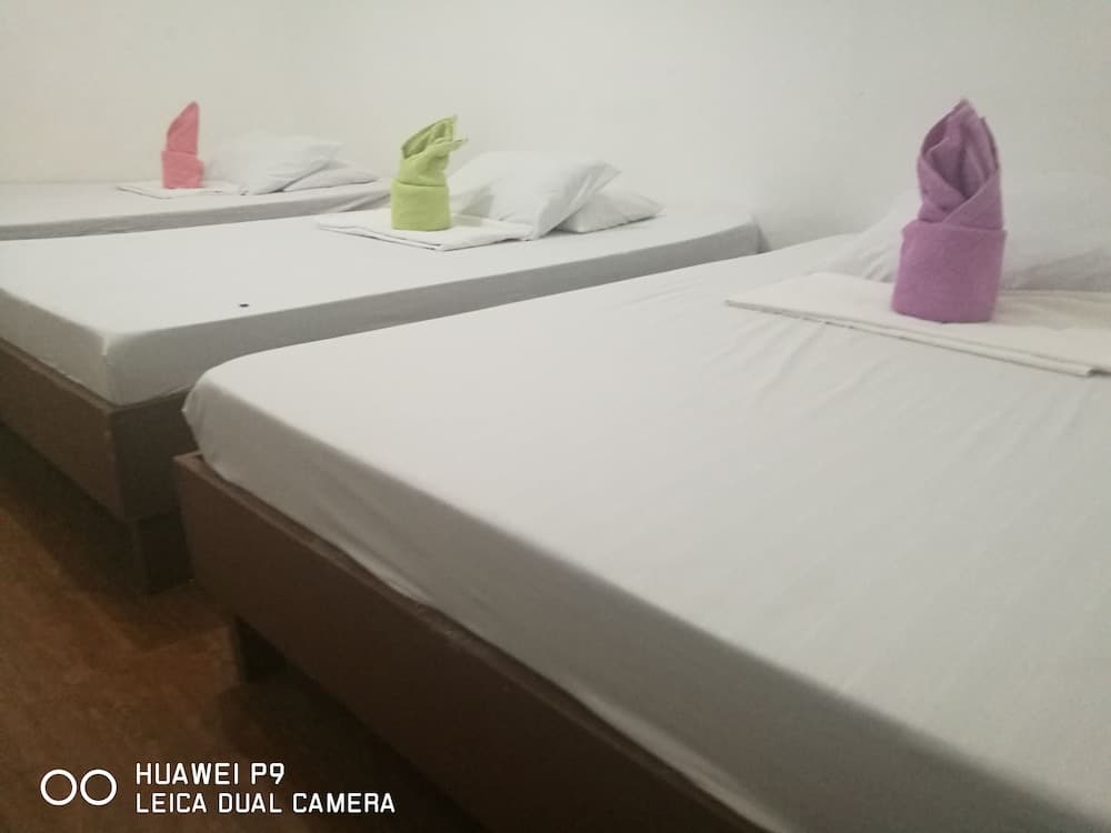 A cozy dormitory-style room features neatly arranged single beds with colorful towel swans, ideal for budget travelers seeking simple accommodations.