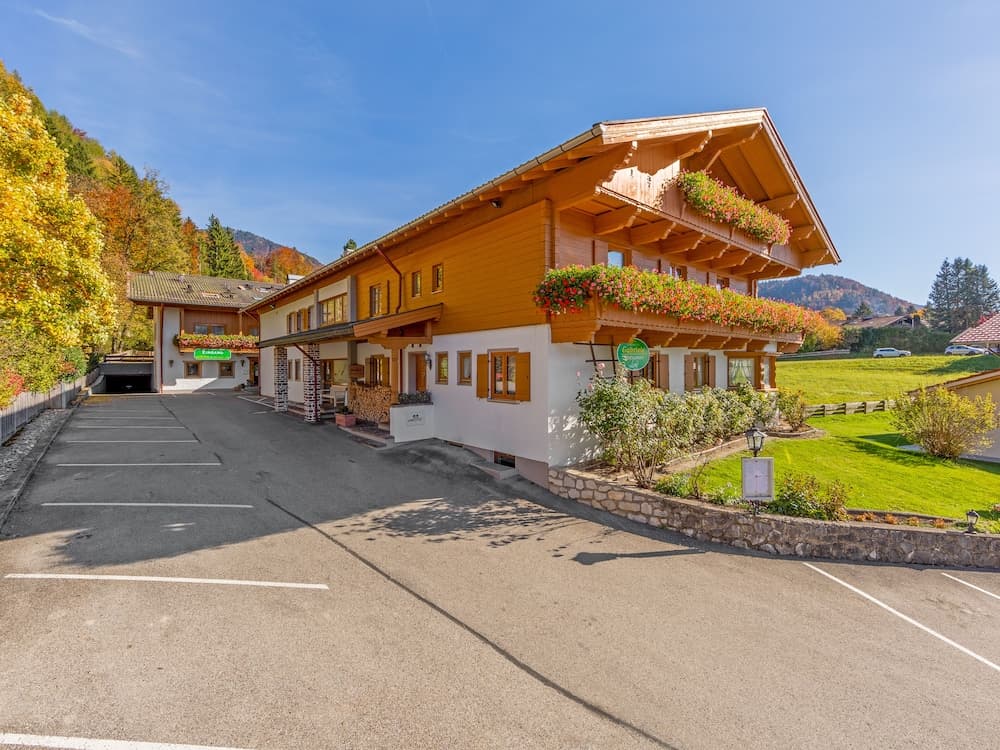 A charming alpine lodge with vibrant flower boxes and a sunny parking lot invites travelers to a serene mountain retreat perfect for autumn getaways.