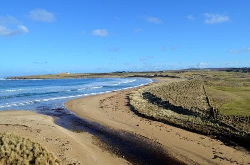 A serene coastal landscape features a sandy beach meeting calm blue waters under a clear sky, ideal for tranquil beachside relaxation and scenic photography.