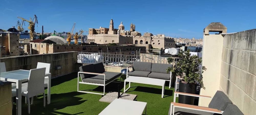 A serene rooftop terrace with modern seating overlooks historic architecture and cranes under a clear blue sky, ideal for travelers seeking a relaxing urban retreat.
