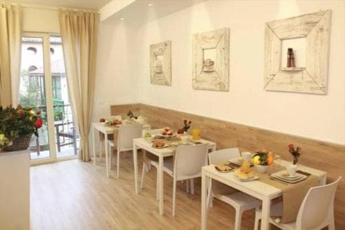 A cozy indoor dining area with white tables set for breakfast, adorned with fresh flowers and framed artwork, offers a serene and inviting atmosphere ideal for travelers seeking a comfortable stay.