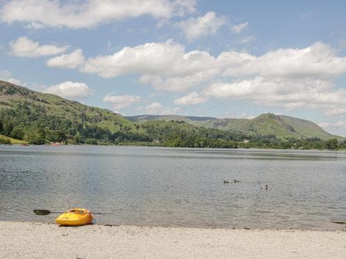 A serene lakeside scene with a yellow kayak resting on the shore under a partly cloudy sky, ideal for tranquil water activities in a picturesque natural setting.