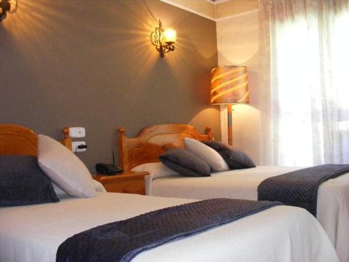 A cozy hotel room features two neatly made beds with wooden headboards, soft lighting from wall sconces, and a warm ambiance, ideal for travelers seeking comfort and relaxation.