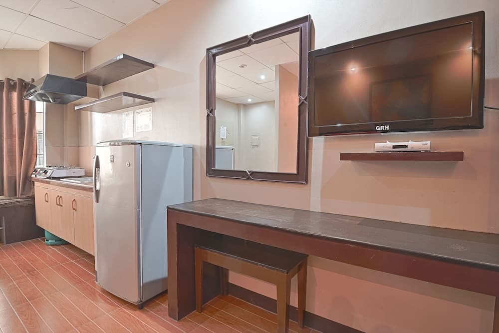 A cozy hotel room corner features a compact kitchenette with a refrigerator, stove, and sink, complemented by a wooden desk with a mirror and mounted TV, ideal for travelers seeking convenience and comfort.