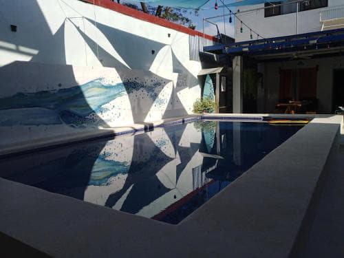 A serene poolside retreat features a vibrant mural of ocean waves on a white wall, creating a tranquil atmosphere ideal for relaxation at a cozy vacation rental.