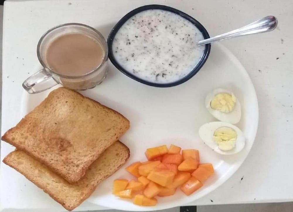A simple breakfast scene featuring toast, papaya chunks, boiled eggs, a bowl of yogurt, and a cup of tea on a white plate, ideal for travelers seeking healthy and affordable dining options.