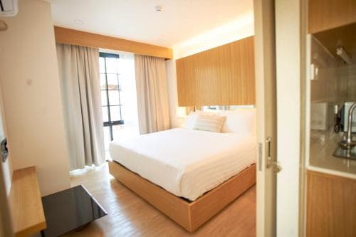 A cozy hotel room with a neatly made bed, wooden furnishings, and a bright window, evokes a serene and inviting atmosphere ideal for travelers seeking comfort and relaxation.