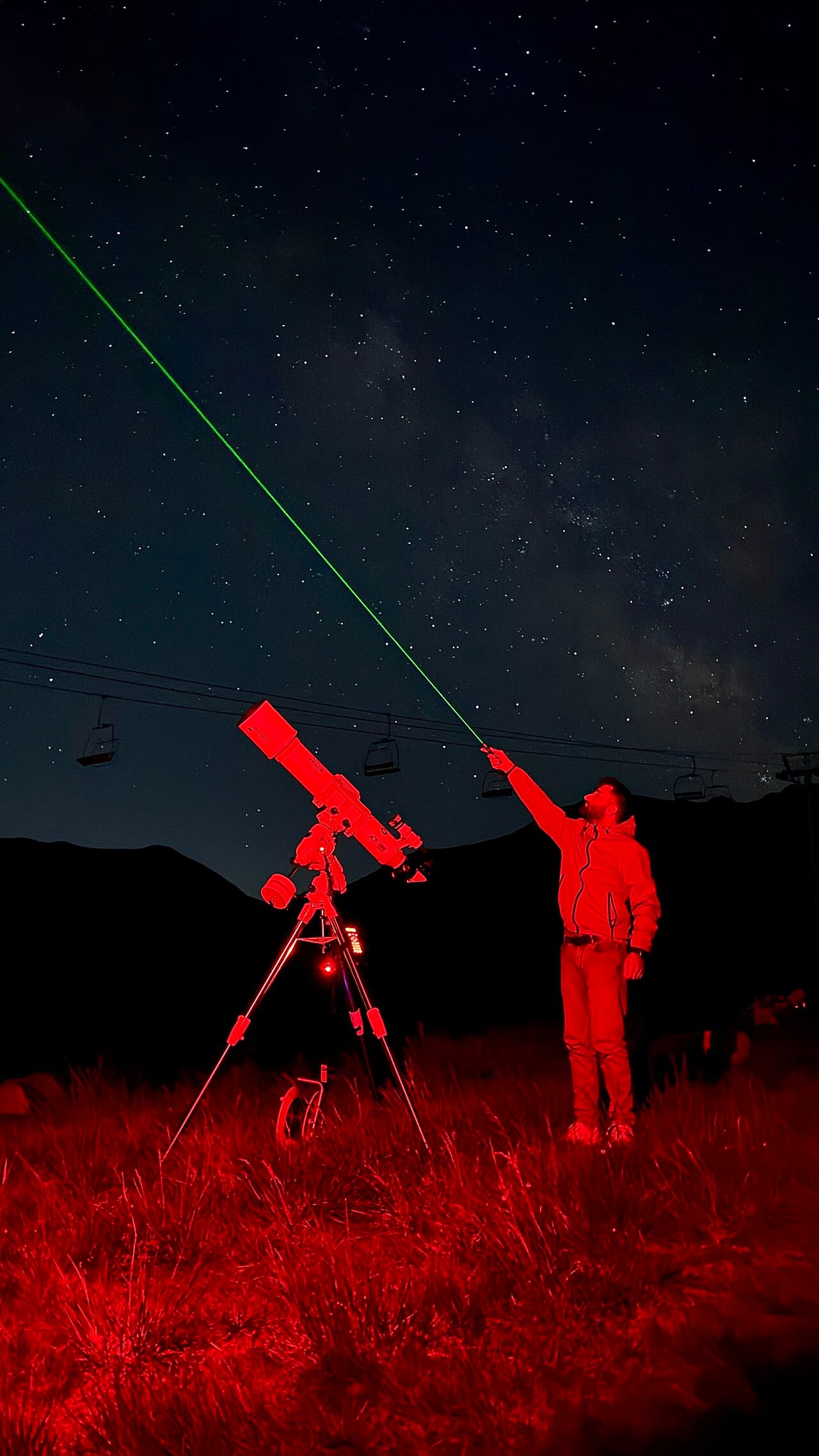 Stargazing tour guide pointing out stars beside a telescope under a dark sky